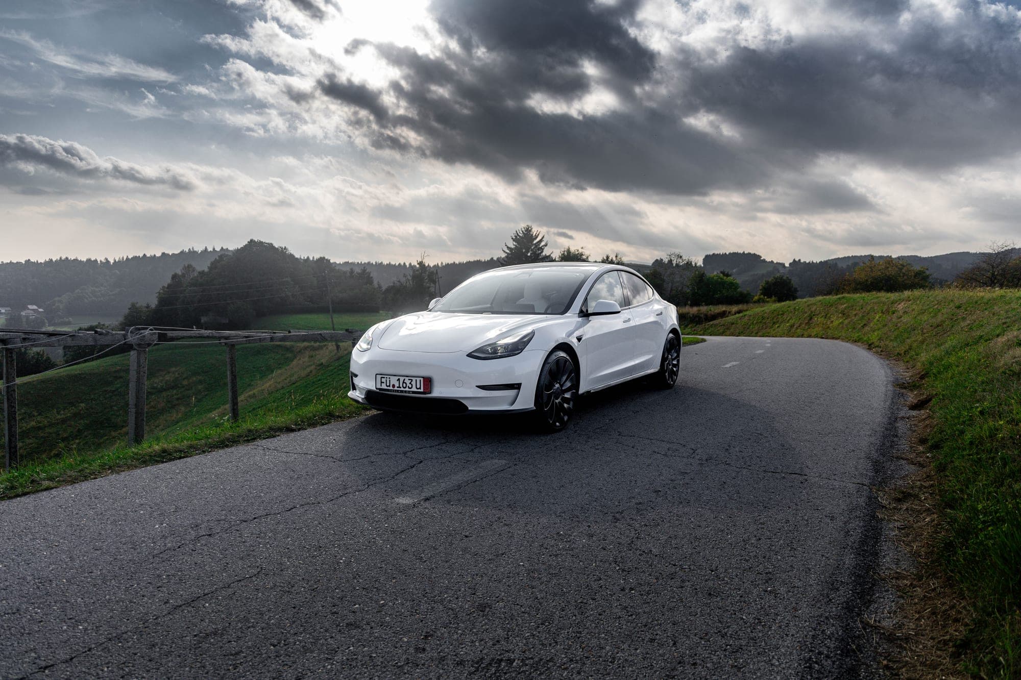 Bela Tesla Model 3 na podeželski cesti pod oblačnim nebom